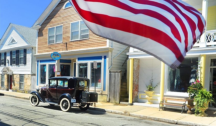 An American flag blows in the wind with a vintage car in background in