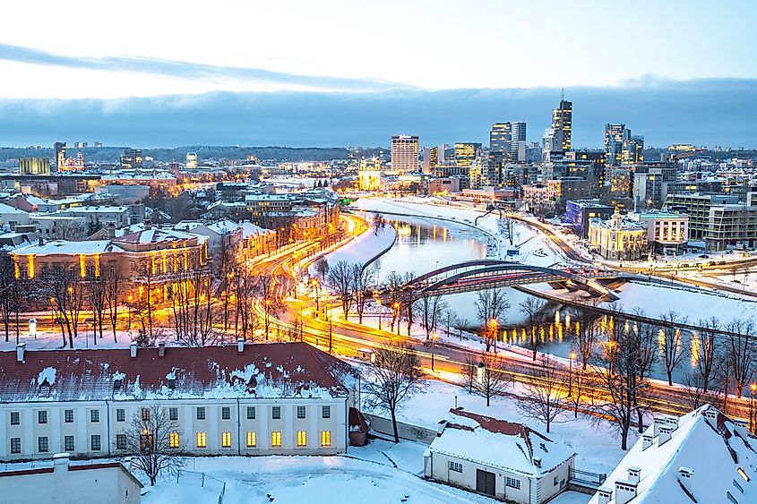 A winter night view of Vilnius showing a glowing cityscape along the Neris River.