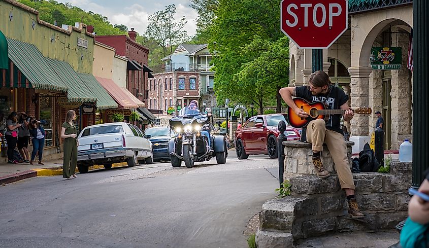 Bikers riding through downtown Eureka Springs, Arkansas, USA. Man playing guitar at stop sign. Vintage small-town Americana scene.