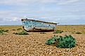 Abandoned fishing boat on a desert pebble beach with plants around in Dungeness, England. Editorial credit: Carina S / Shutterstock.com