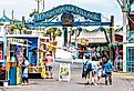 Sign for Harborwalk Village in Destin, Florida with people walking and shopping, buying food in cafe, street vendor restaurants. Image credit Andriy Blokhin via Shutterstock