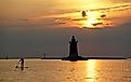 Silhouette of a light house and a man on a paddle board during sunset at Cape Henlopen State Park, Lewes, Delaware.