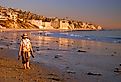 An adult woman walks barefoot on the beach on a fall vacation day on the coast of Laguna Beach, California. Image credit James Kirkikis via Shutterstock