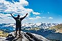 Hiker with arms raised in triumph standing atop a mountain in Rocky Mountain National Park, Colorado.