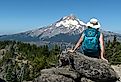 A mature woman hiker sites on a rock with her back to us and enjoys the view of Mt. Hood, Oregon.