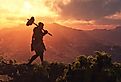 Primitive man walking on the grass with the sun setting.