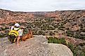 A man sitting on a cliff with his dog while taking a break from hiking the Palo Duro Canyon. 