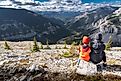 A brother and sister sitting on a rock overlooking the Canadian Rocky Mountains, with a valley of trees displaying fall colors on Moose Mountain near Bragg Creek, Alberta, Canada.