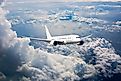 A white passenger jet plane flying high through the cumulus clouds in the blue sky, seen from the front view.