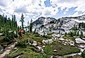 A man in bright orange shirt standing on hiking trail to take picture of beautiful lake and mountain while backpacking in the Enchantments, Leavenworth, Washington. Image credit Suchavadee via Shutterstock.