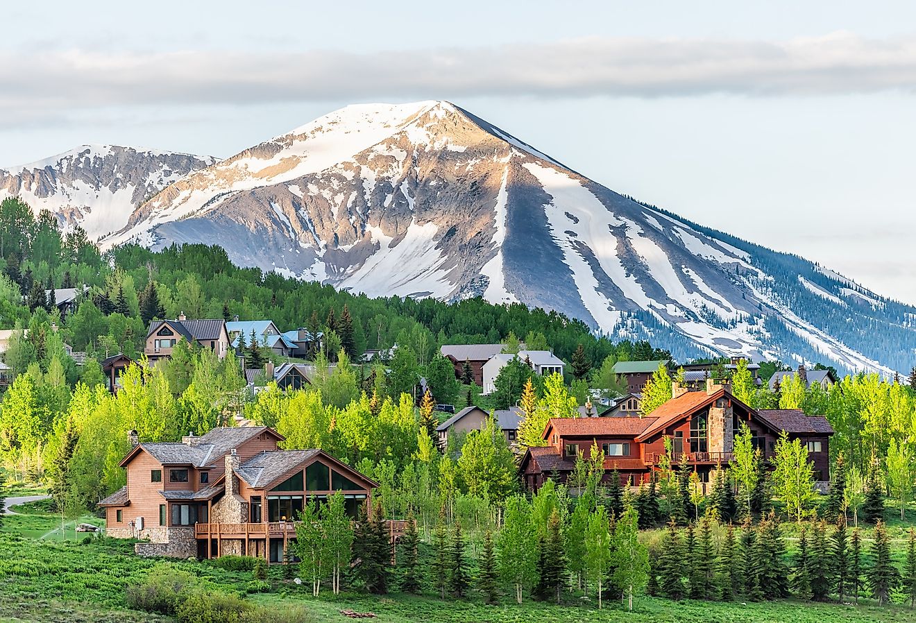 Mount Crested Butte, Colorado village in summer with colorful sunrise by wooden lodging houses on hills with green trees.