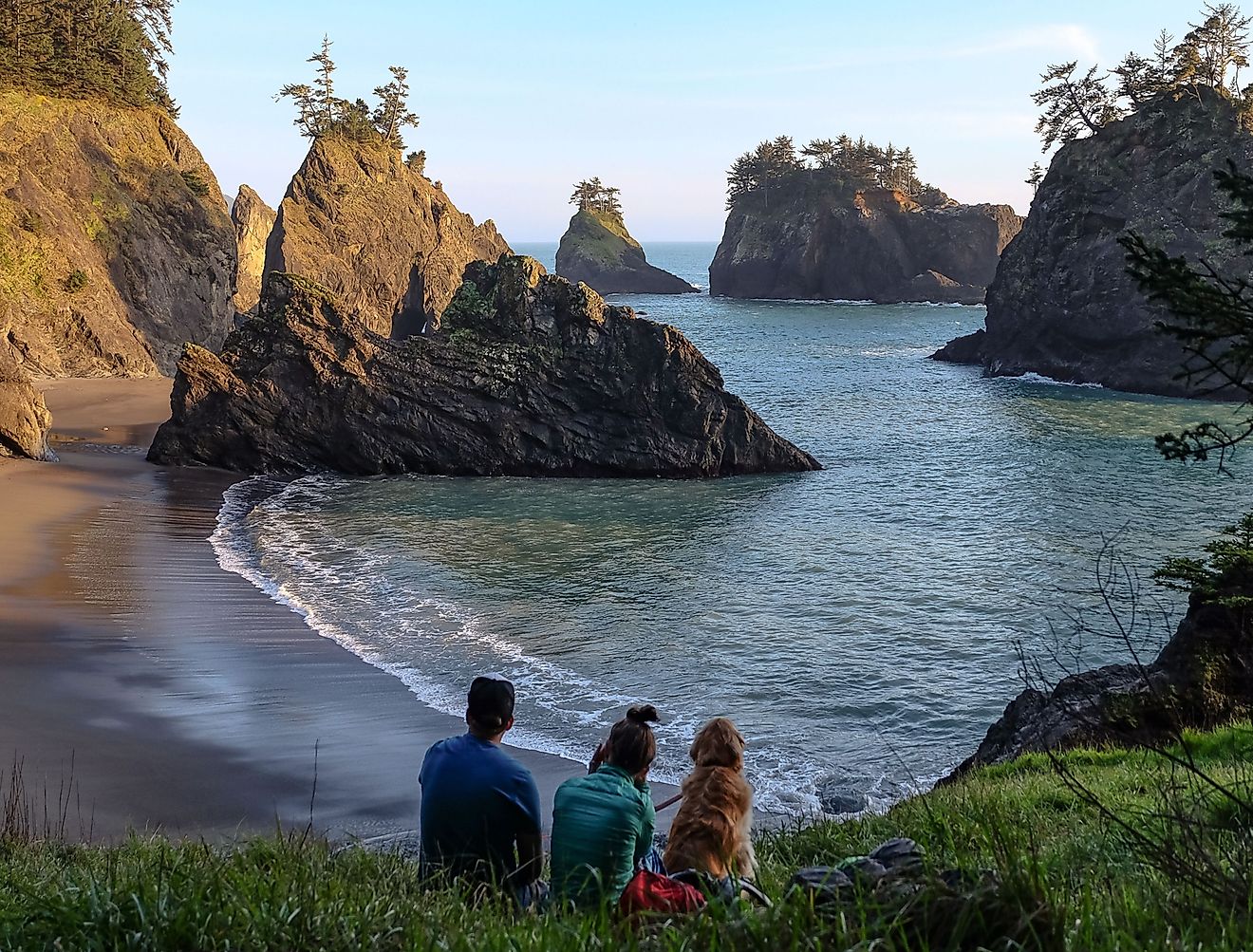 A couple and their dog watch the sunset over Secret Beach in Oregon. Image credit Ashley Hadzopoulos via shutterstock