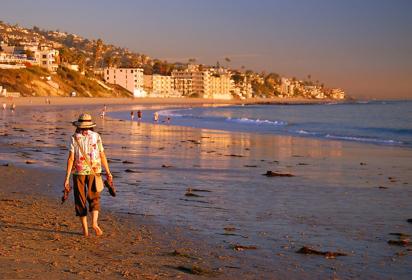 An adult woman walks barefoot on the beach on a fall vacation day on the coast of Laguna Beach, California. Image credit James Kirkikis via Shutterstock