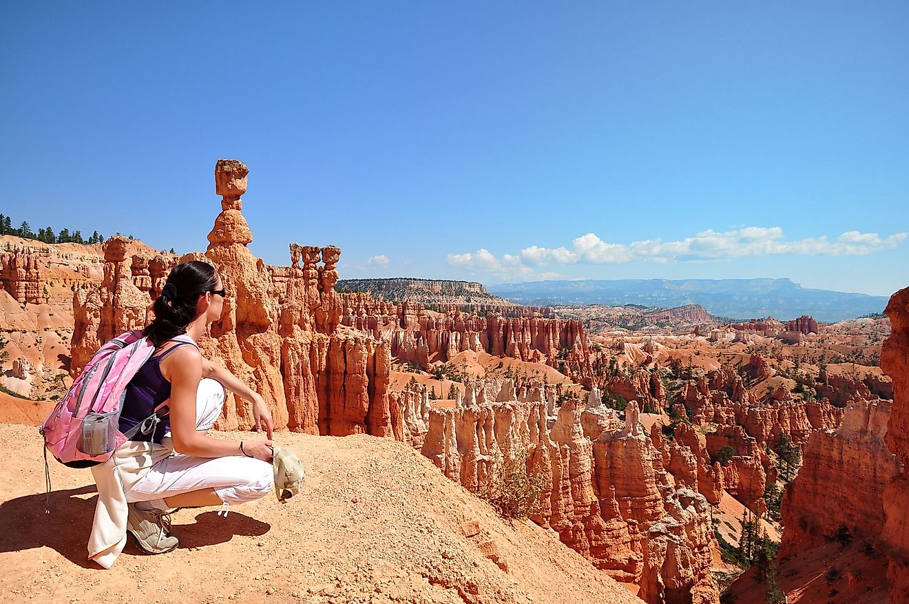 A woman hiking wearing a pink backpack kneels to view the panorama of Bryce Canyon in Utah. 