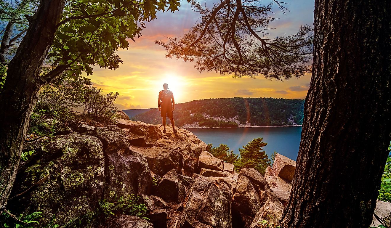 A silhouette of a man looking out into the sunset over Devils Lake State Park from a hiking viewpoint in Baraboo, Wisconsin USA.