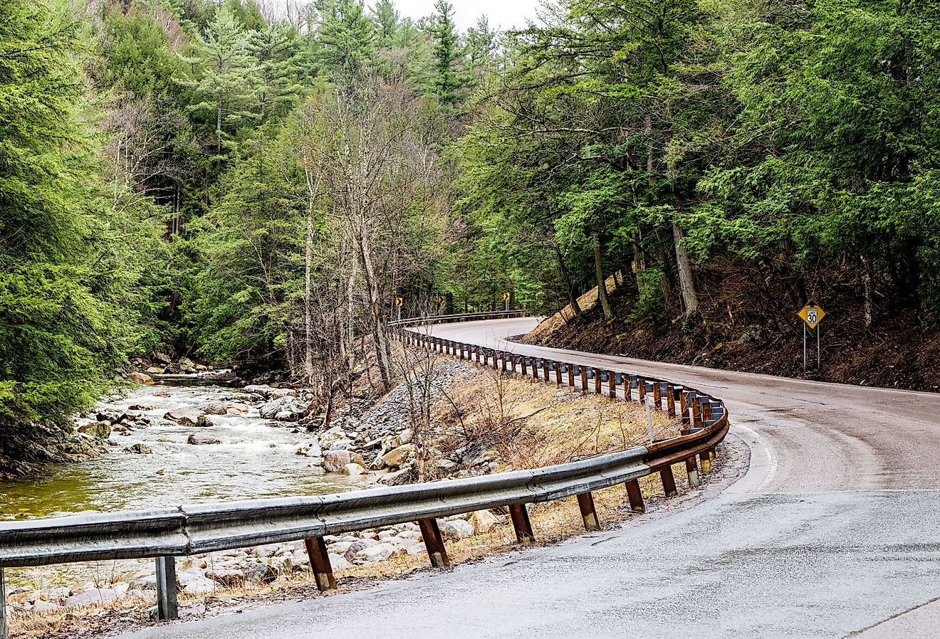 A narrow road curves beside a rushing stream at the eastern edge of the Adirondack Mountains in northeast New York.