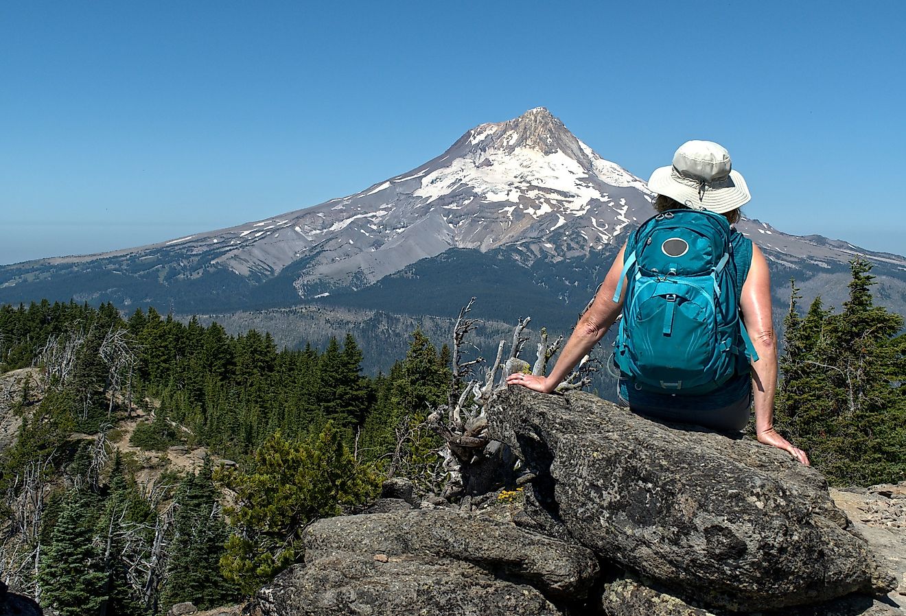 A mature woman hiker sites on a rock with her back to us and enjoys the view of Mt. Hood, Oregon.