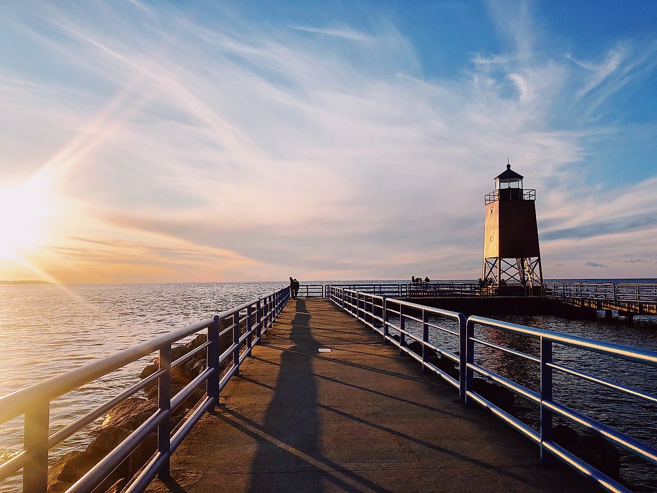 Sunset view of the lighthouse and pier in Charlevoix, Michigan, with the sky painted in warm hues reflecting on the water