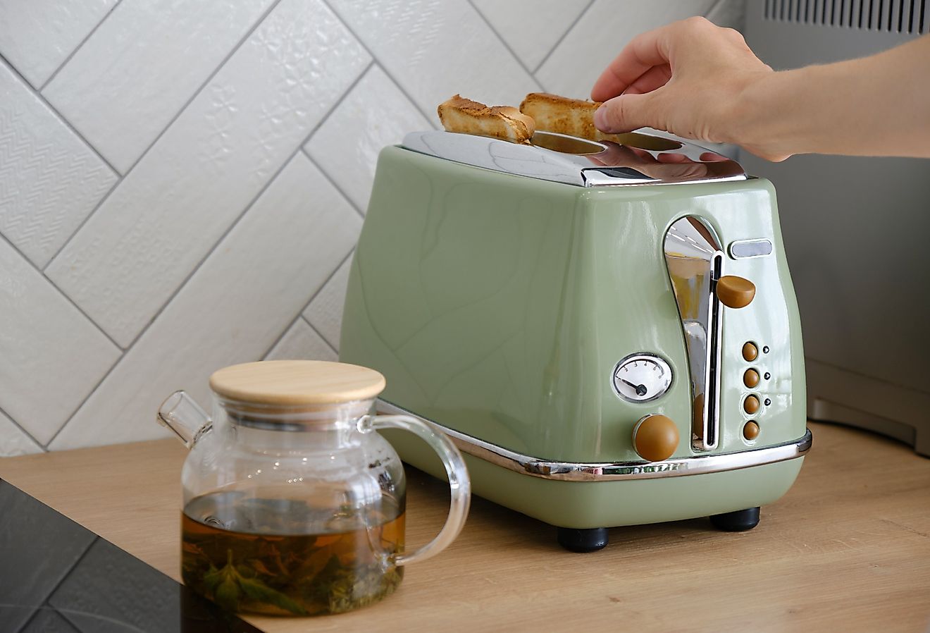 Woman using a retro green toaster on the countertop with a cup of tea.