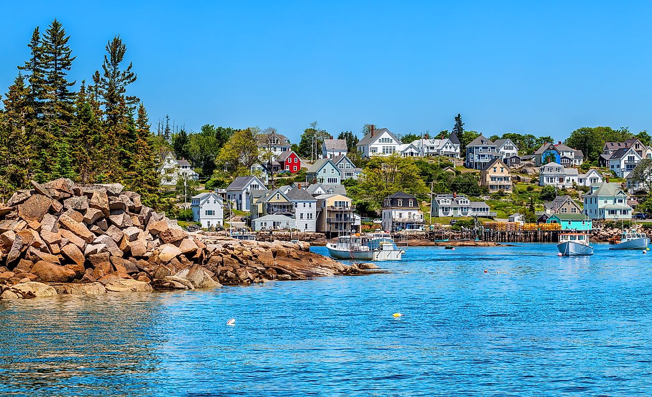 The picturesque waterfront and harbor of Stonington, Maine, featuring classic New England fishing boats, docks, and seaside cottages, all set against a backdrop of rocky shores and calm waters.