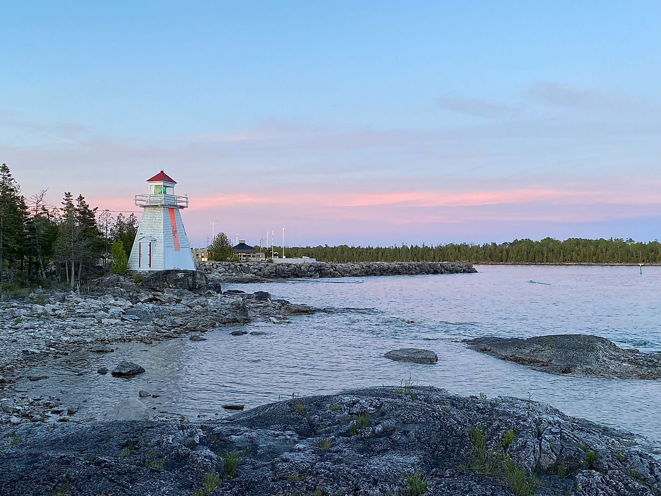 A rustic lighthouse welcomes boats to the south side of Manitoulin Island. A pink, post-sunset sky compliments the rocky Niagara Escarpment and deciduous trees