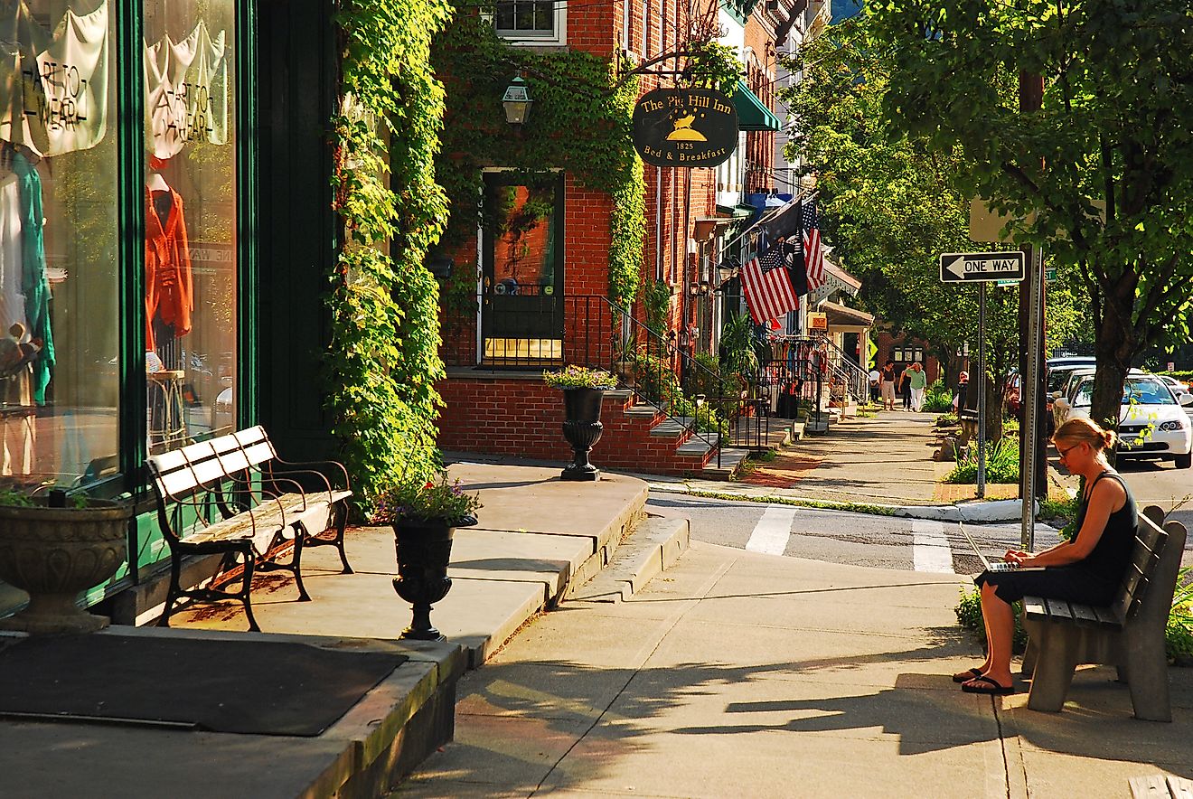 A young woman works on a laptop sitting on a bench in downtown Cold Spring, New York, James Kirkikis / Shutterstock.com