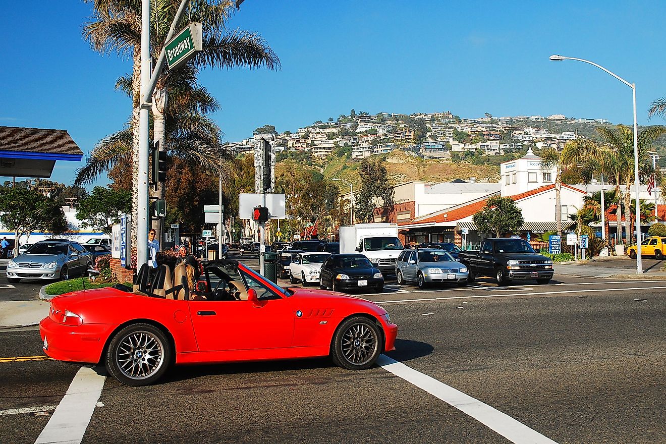 A woman driving a red convertible cruises through the shopping district of Laguna Beach, California