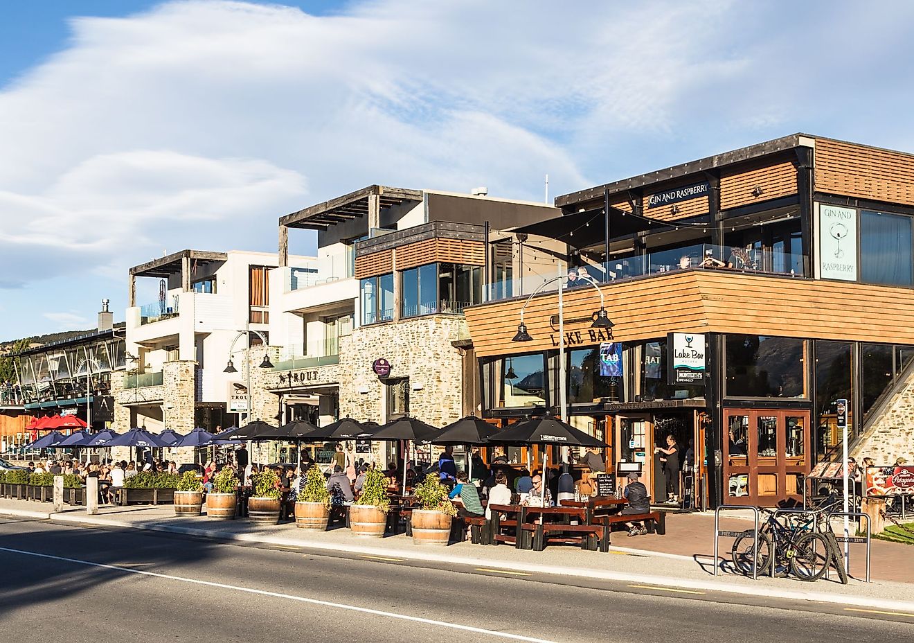 Tourists and locals enjoy a drink on the trendy sidewalk bar and restaurants in Wanaka lakefront in Wanaka, New Zealand. Editorial credit: AsiaTravel / Shutterstock.com