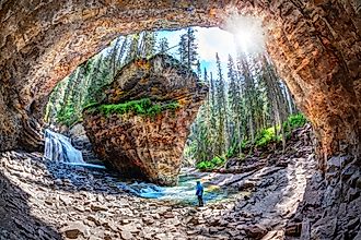 Hiker stands in awe of waterfall and limestone bedrock at a hidden cave in Johnston Canyon at Banff National Park.