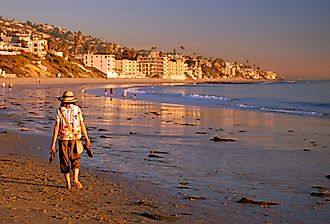 An adult woman walks barefoot on the beach on a fall vacation day on the coast of Laguna Beach, California. Image credit James Kirkikis via Shutterstock