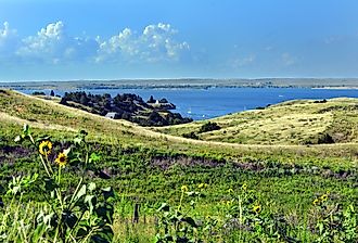 Rolling Nebraska grassland slopes down to the blue small bay with tiny white sail boats on Lake McConaughy.