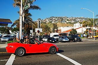 A woman driving a red convertible cruises through the shopping district of Laguna Beach, California