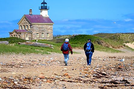 women walk the shoreline past the historic North Lighthouse on Block Island. Editorial credit: Ray Geiger / Shutterstock.com