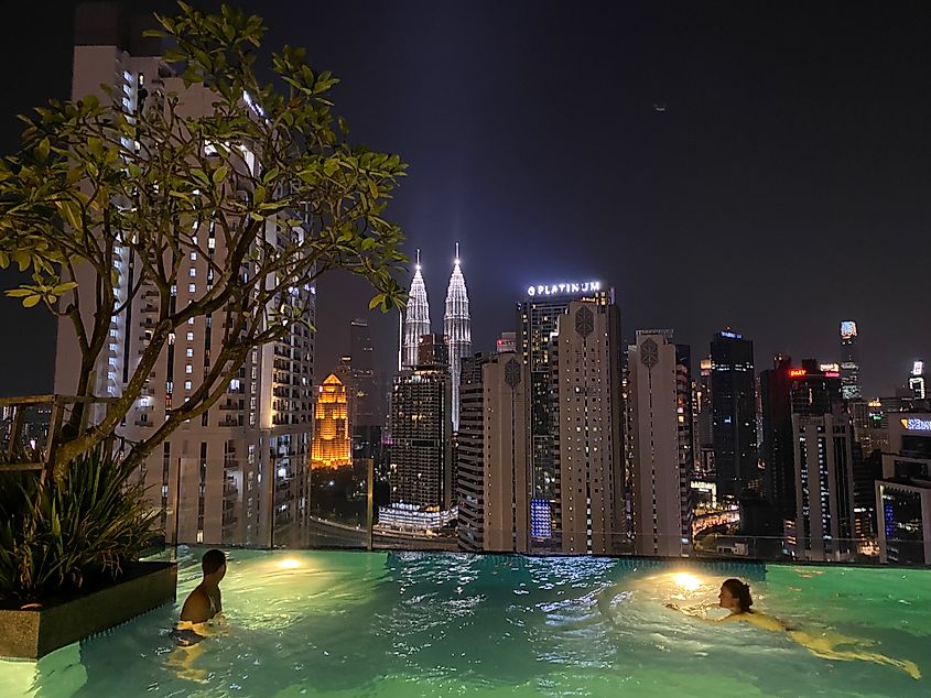A hotel rooftop pool looks out over the iconic buildings of Kuala Lumpur at night.