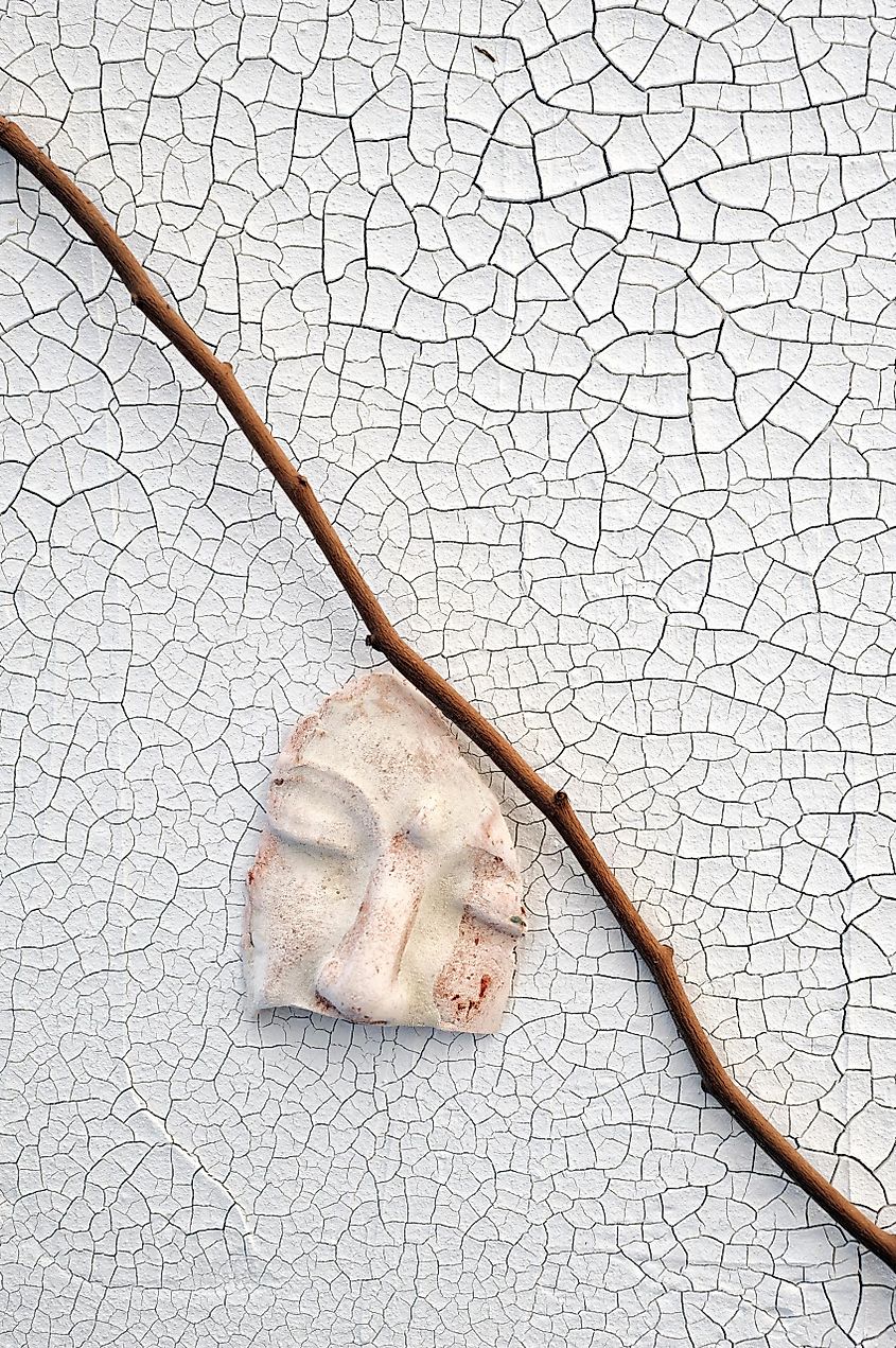 Conceptual art. A bleeding white mask and stick on a cracked surface