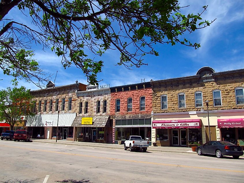 Historic downtown street with colorful brick storefronts under a clear blue sky. Trees frame the scene, creating a quaint and vibrant atmosphere.