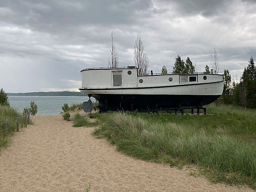 A weathered white sailboat sits in dune grass just off the waters of Lake Michigan.