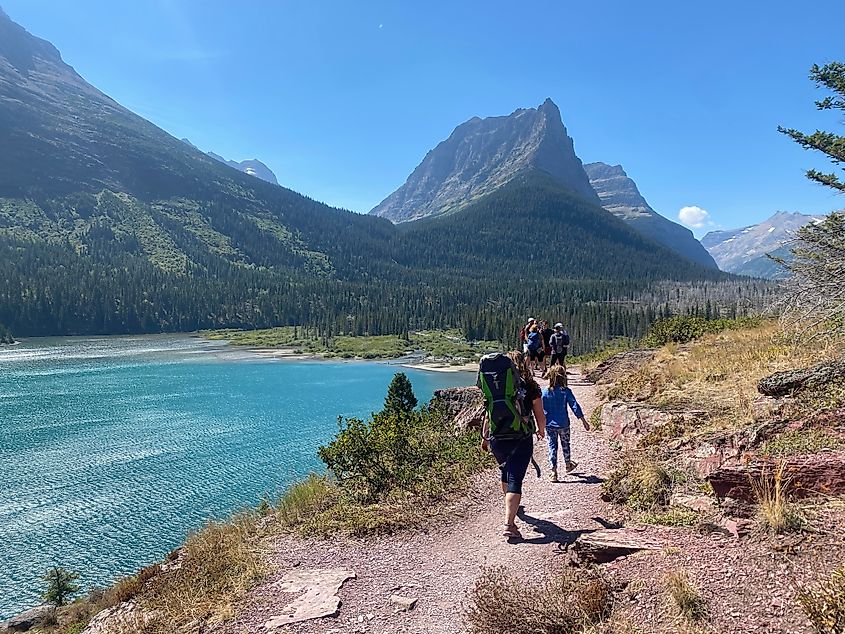 A group of hikers walking on three falls trail with Saint Mary Lake below and the mountains in the background, in Montana, USA. Glacier National Park, Montana, United States. Editorial credit: christopher babcock / Shutterstock.com