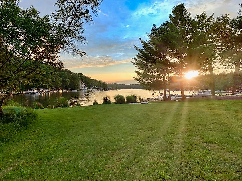 Sunset over Lake Harmony, PA, sun peeking through the trees and reflecting off the water against a blue sky.