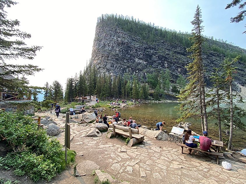 Modest crowds gather around an alpine lake. A rustic wooden tea house just comes into frame. 