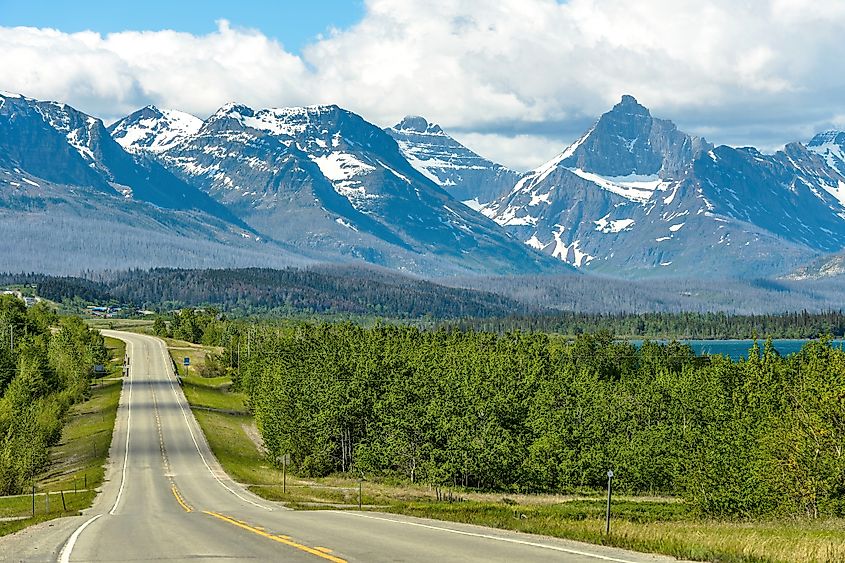 A cloudy spring morning view of a winding road (U.S. 89) extending towards snow-capped high mountain peaks in Glacier National Park, Montana