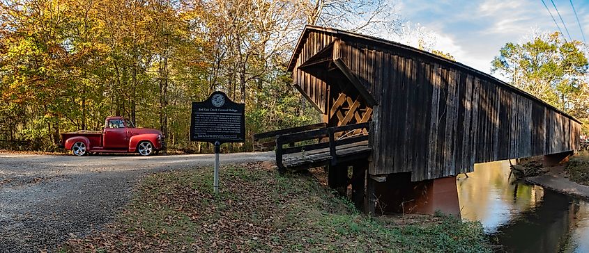 Panoramic view of a vintage red truck next to the historic Red Oak Creek Covered Bridge in Woodbury, Georgia