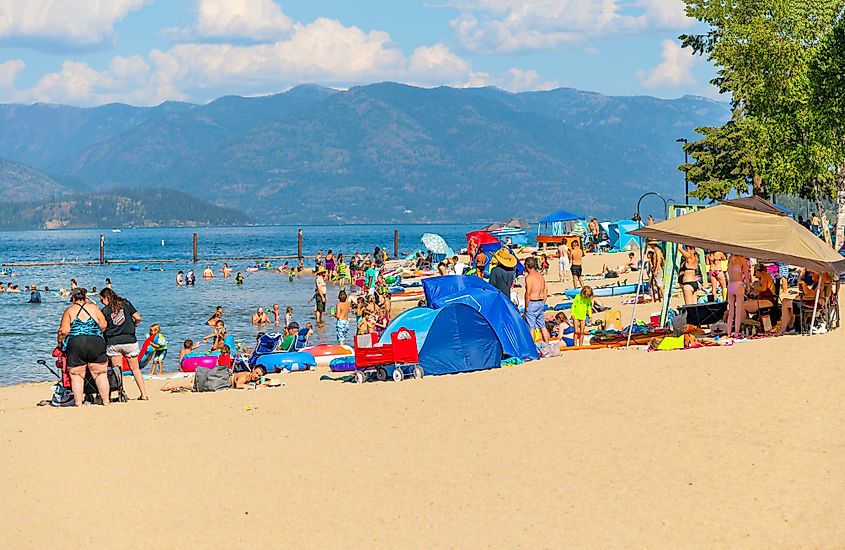 Sunny summer day at the crowded city beach in downtown Sandpoint, Idaho, with tourists and locals enjoying the atmosphere.