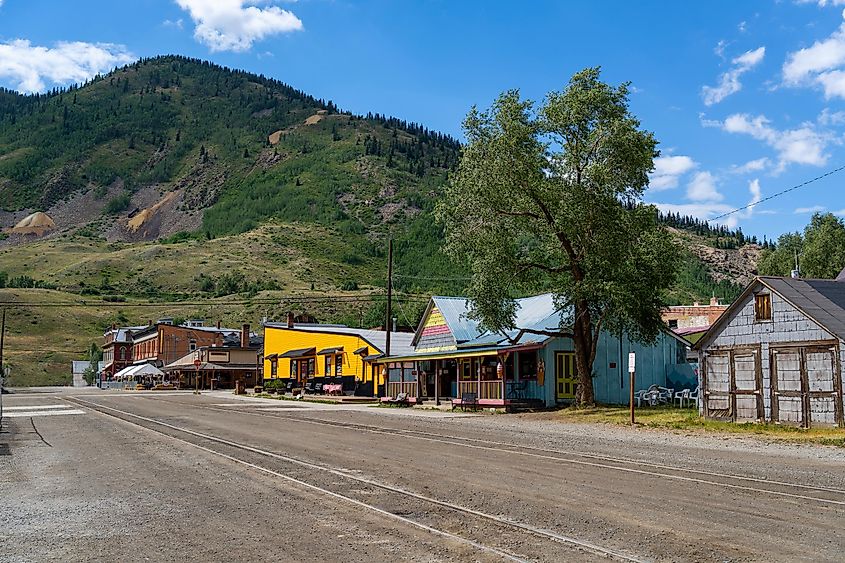 A strip of old style wooden and brick buildings along an old town street with trees and mountains in the background, Silverton, Colorado.