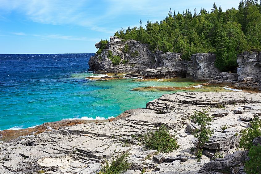 Forested limestone cliffs meet a pebble beach and turquoise waters