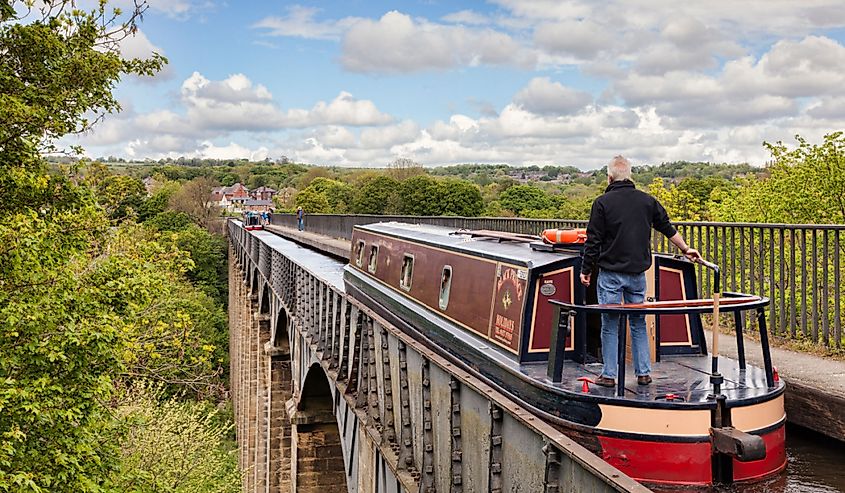 Man at tiller, steering narrowboat over the Pontcysyllte Aqueduct in Llangollen, Denbighshire