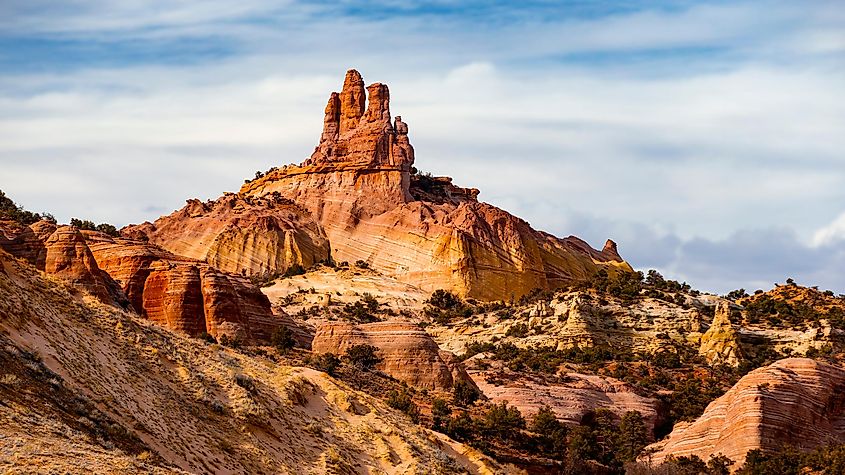 Majestic red rock formations under a partly cloudy sky in a desert landscape. The layered cliffs, rich in earthy tones, evoke a sense of awe and grandeur.