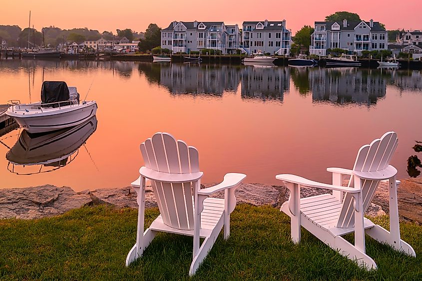Two white chairs on the beach overlooking the Mystic River marina village in Connecticut