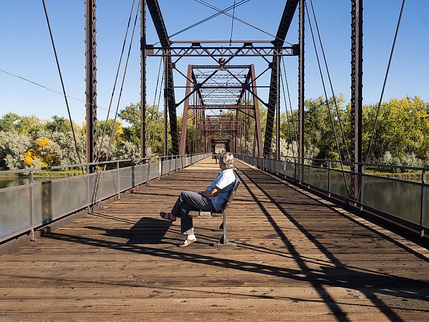 A senior woman sitting on a bench on the historic Fort Benton Bridge, spanning the Missouri River in Montana