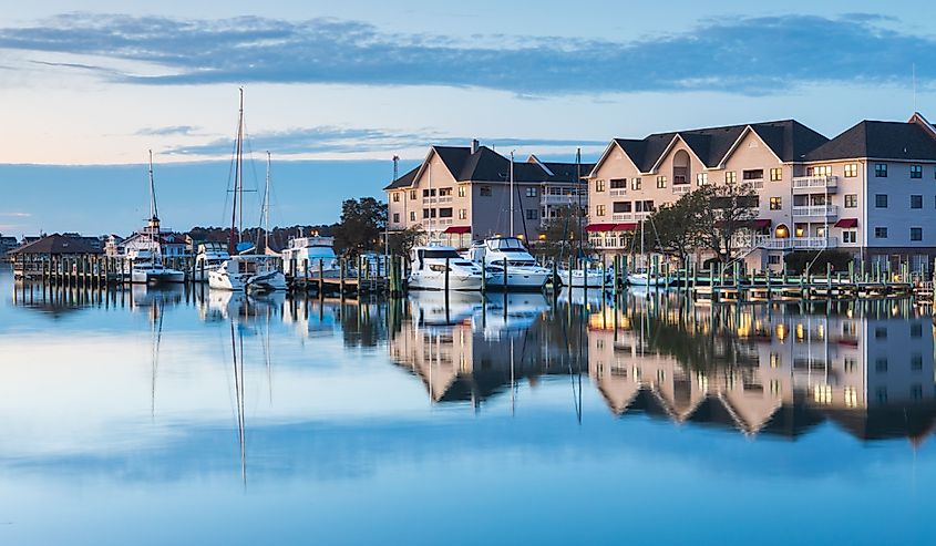  Daybreak over Manteo's waterfront marina in the Outer Banks, North Carolina, showcasing tranquil waters and moored boats under a pastel sky.